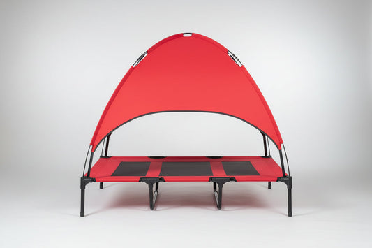 Dog lying on a red pet canopy bed in a home setting with a brick wall and plant in the background.