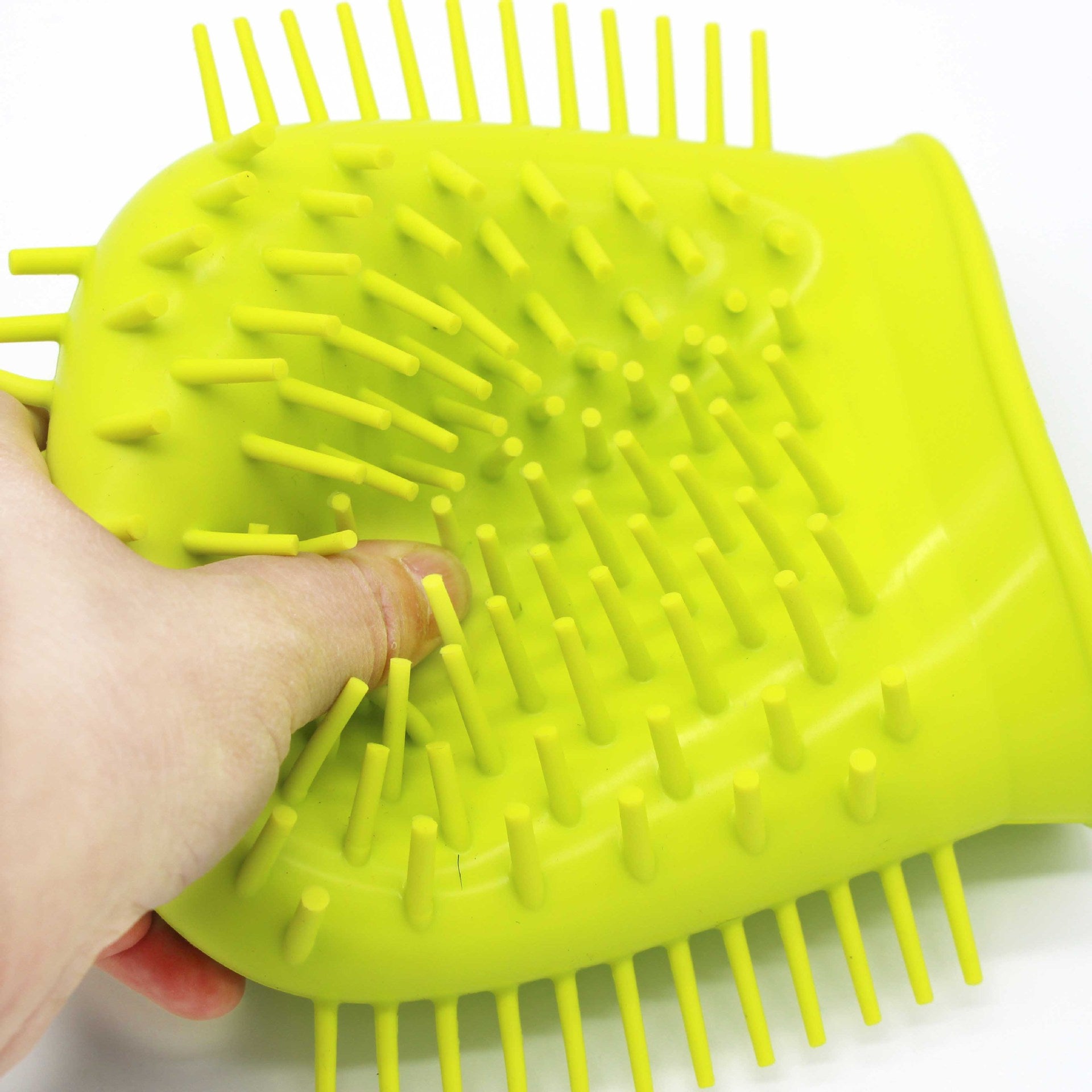 Green silicone brush held by a hand on a white background
