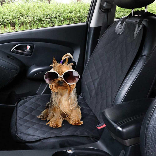 Dog wearing sunglasses sitting on a car seat cover inside a vehicle.