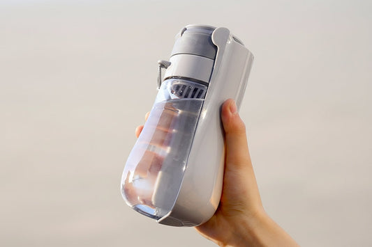 Hand holding a transparent water bottle with text about its wear-resistant and drop-resistant properties.