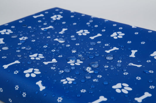 Dog sitting on a blue car bench cover with bone and paw pattern in a vehicle.